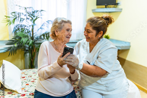 Obraz na płótnie Nurse assisting elderly woman with smartphone in nursing home w salonie