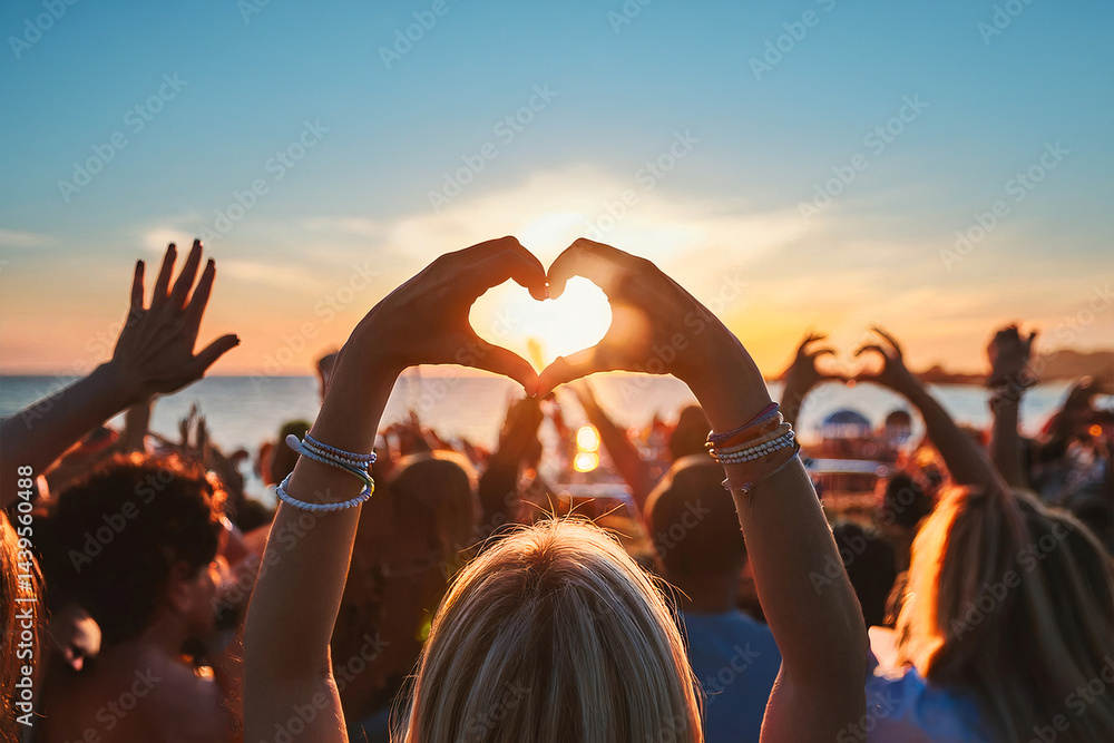 Obraz premium Cheering crowd of young people at beach music festival during sunset with hands forming heart shape