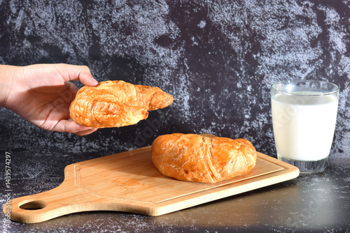A woman's hand holds a glass of milk and a croissant is placed on it. Croissants and milk, homemade morning dayly breakfast on dark wall texture with copy space.