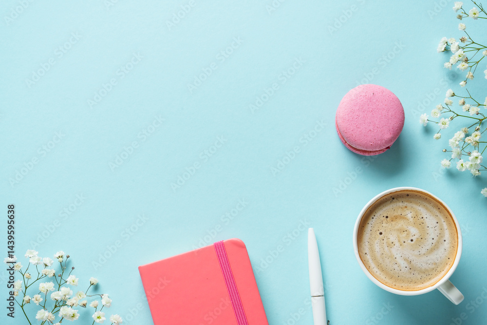 Cup of coffee, macaroon and flower on blue background. Top view with copy space.