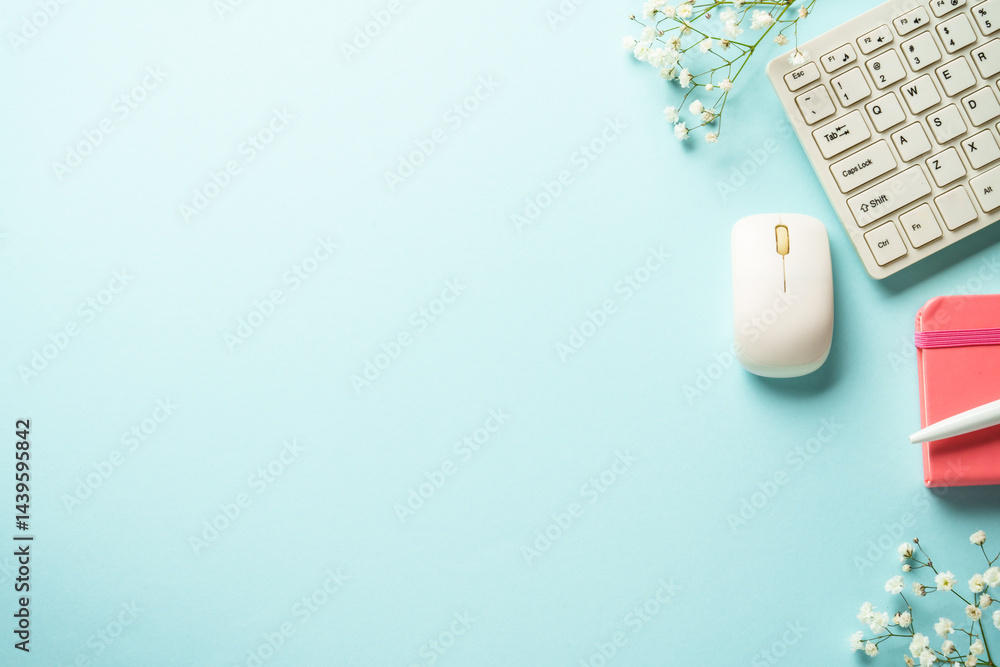 Office desk with keyboard, notebook, pen and flowers on blue background. Flat lay with copy space.
