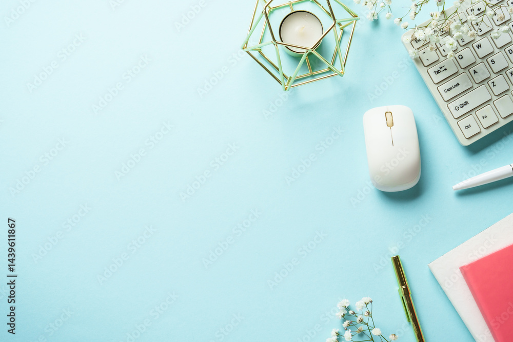 Office table with keyboard, notebook, pen and flowers on blue background. Top view with copy space.
