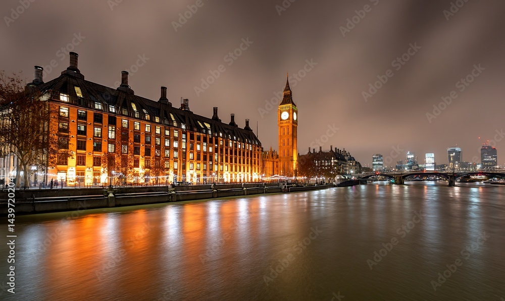 Fototapeta premium Night view of the Houses of Parliament, London, with the River Thames reflecting the city lights. Possible use Stock photo for travel brochures, city guides, or online travel advertising