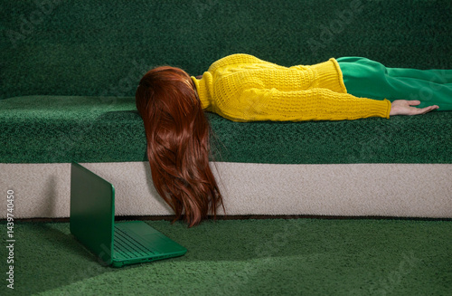 Red-haired woman lying on a couch at home with a laptop, appearing tired and resting.