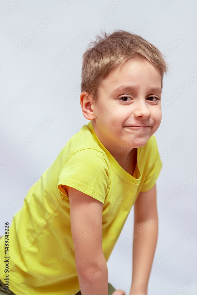 Naklejka premium Smiling young boy with short brown hair wearing a bright yellow t-shirt, leaning slightly forward. His expression is playful and curious, with a dimple visible on his cheek