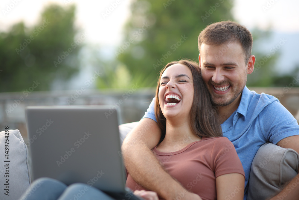 Happy couple laughing watching media on laptop in a terrace Happy couple laughing watching media on laptop in a terrace