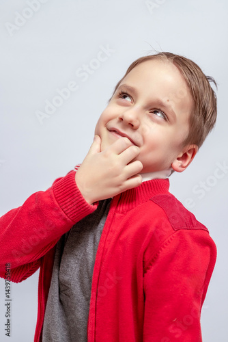 Wallpaper Mural Young boy wearing a red sweater and gray shirt, looks upward thoughtfully with his hand on his chin, displaying a playful and curious expression, light colored background Torontodigital.ca