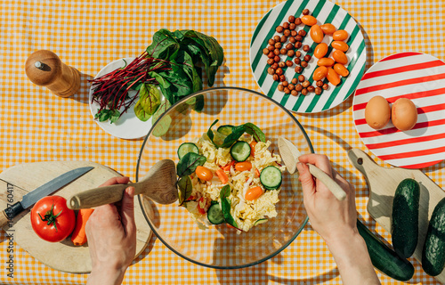 Woman preparing a summer salad with fresh vegetables and ingredients on a gingham tablecloth