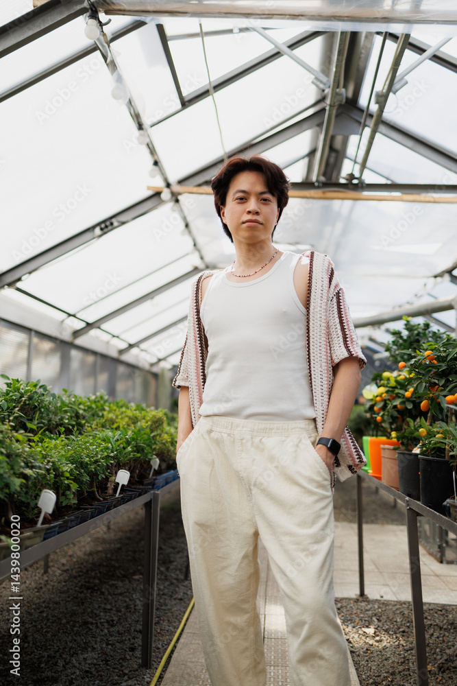 Obraz premium Asian florist looking at camera near bonsai trees in greenhouse