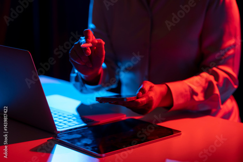 Businesswoman holding a cellphone while touching or pointing at something with a marker. Laptop computer and tablet on the table. Mockup and copy space. Business and technology concept.