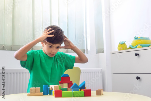 Фотография Tired little boy covering face with hands after playing with wooden blocks, expe