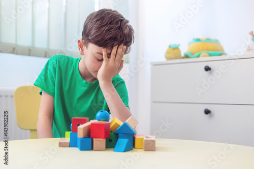 Tableau sur toile Tired little boy covering face with hands after playing with wooden blocks, expe