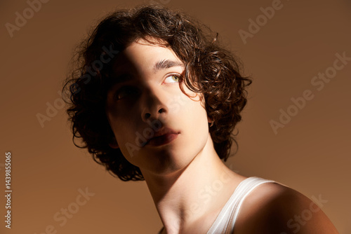 Fotografie Stylish young man with curly hair posing in a studio during golden hour lighting