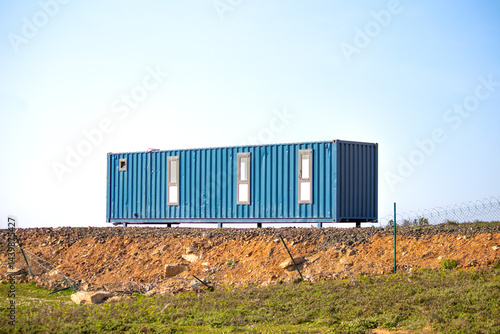 Container house on blue sky background. Tiny house idea concept. Minimalist lifestyle. Life in the countryside. Sustainable, eco friendly or holiday accommodation. Copy space, blank.
