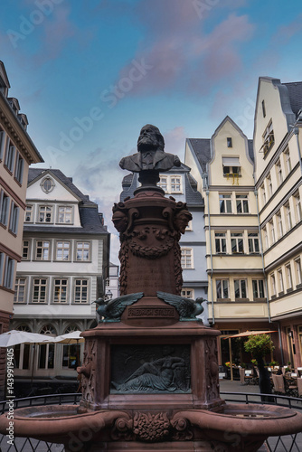 Obraz na płótnie Statue of Friedrich Schiller atop an ornate fountain with intricate carvings, surrounded by European style buildings under a partly cloudy sky in Frankfurt. w salonie