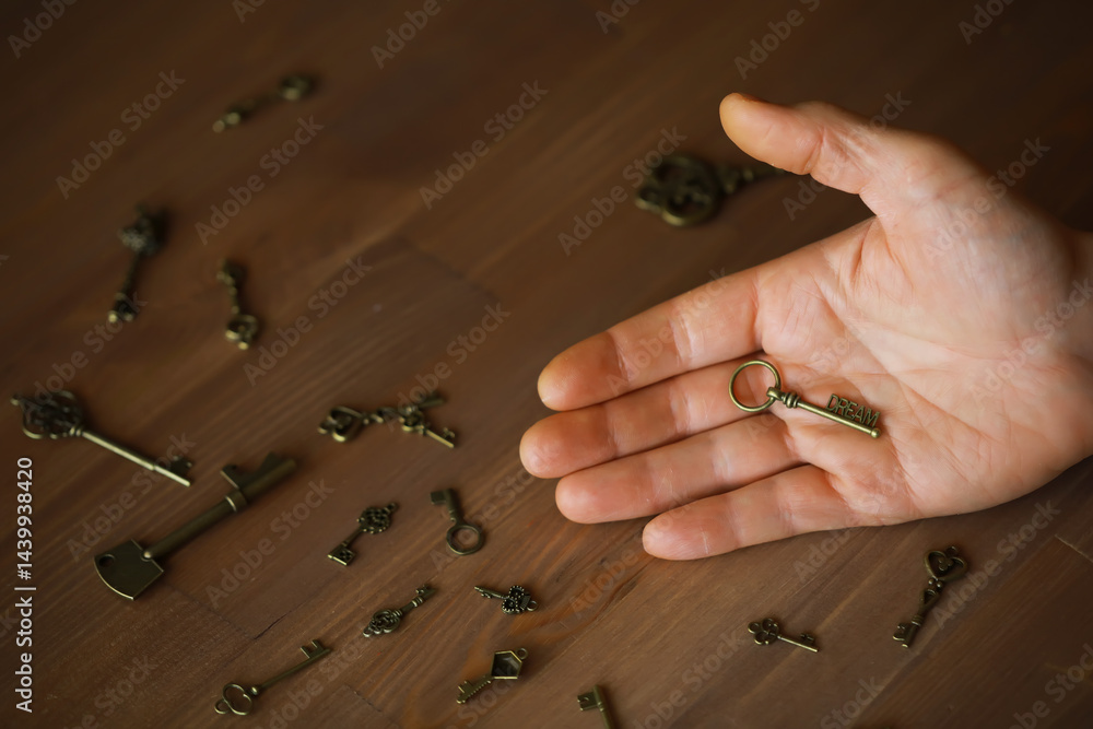 Hand Holding a Single Antique Key Amongst a Collection of Vintage Keys on Wooden Surface