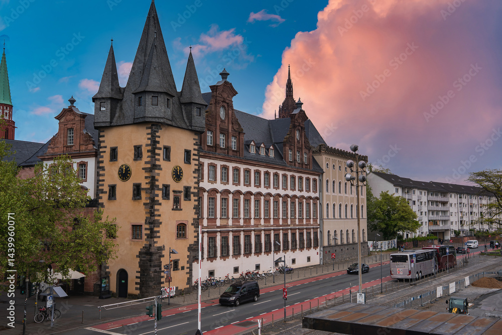 The Saalhof building in Frankfurt, Germany, features medieval architecture with pointed towers and a clock, set near a busy street with cars and buses.