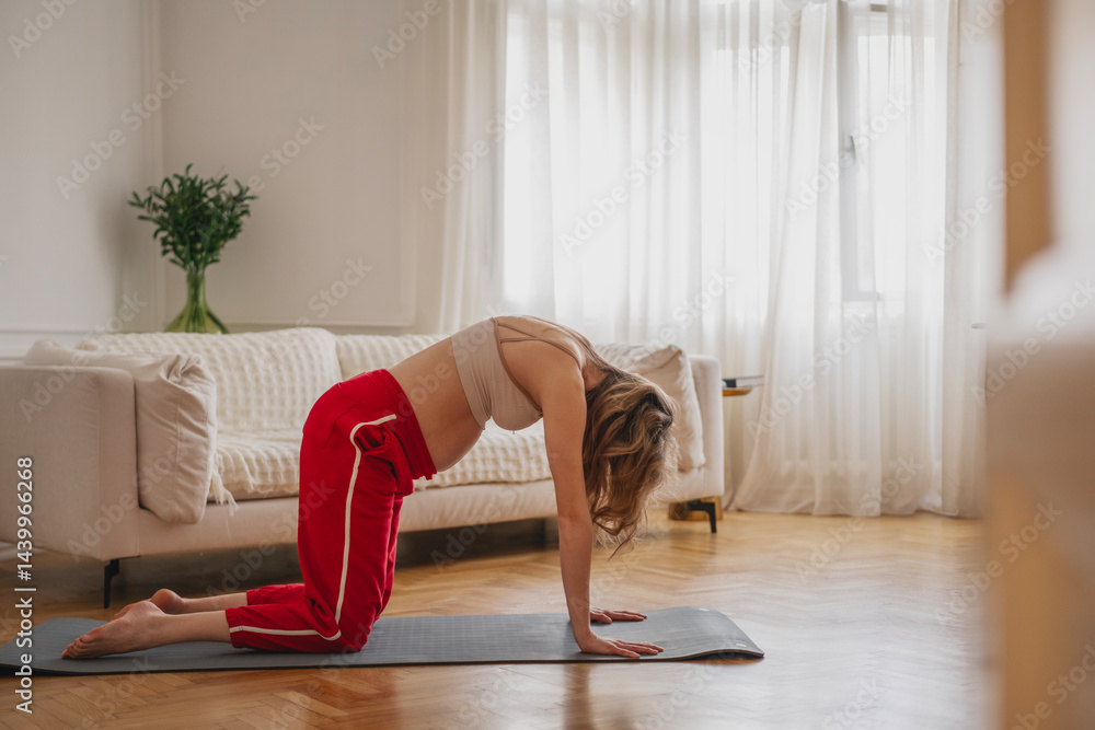 Young caucasian pregnant woman doing yoga and stretching at home in living room