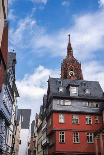 A street in Frankfurt, Germany, featuring half timbered buildings with vibrant facades and the Gothic spire of Frankfurt Cathedral under a blue sky.