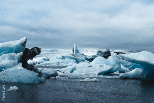 Dramatische Aufnahme eines schroffen Eisbergs in der Gletscherlagune Jökulsárlón in Island. Das gefrorene Wasser und die bläulichen Eisskulpturen stehen im Kontrast zum grauen Himmel.