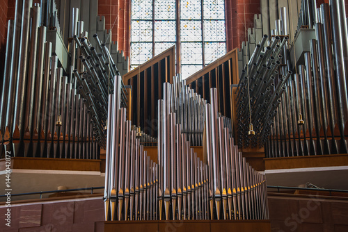 Obraz na płótnie A grand pipe organ with intricate metal pipes stands before a large stained glass window. Red brick walls and wooden details highlight the historic interior. w salonie