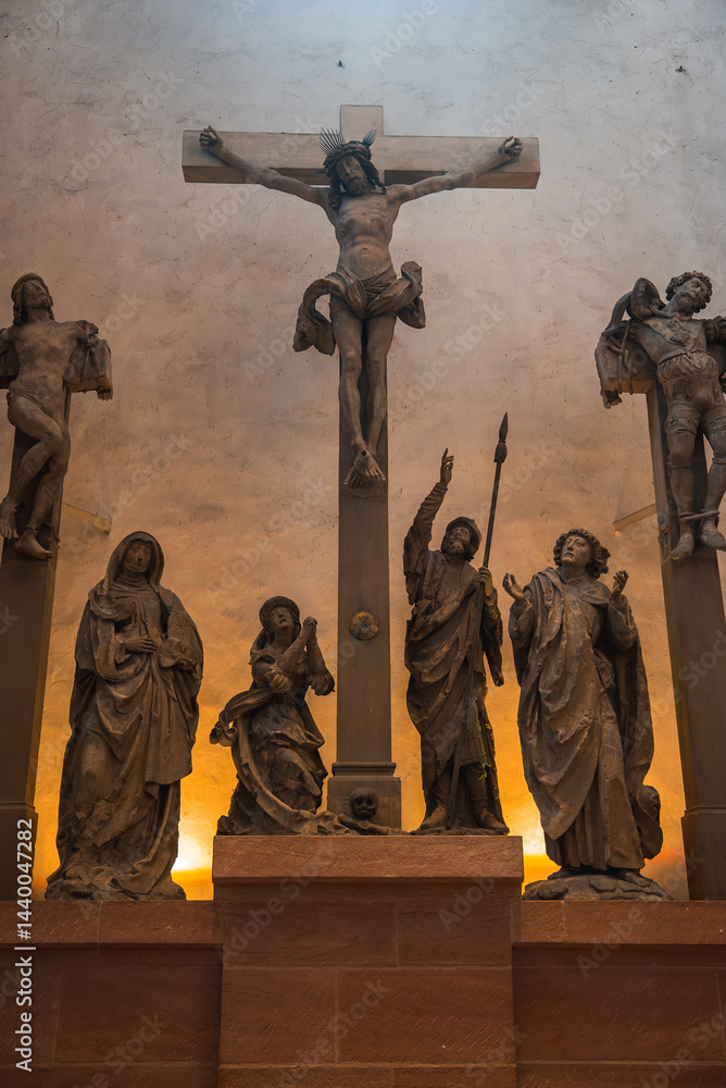Detailed crucifixion sculpture with Jesus Christ, mourners, and saints in a church in Frankfurt, Germany, illuminated with a warm glow.