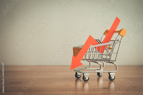 Shopping trolley with red chart falling down on wooden table white wall background copy space. Economic recession crisis, core retail sales decrease, inflation or goods price up concept.