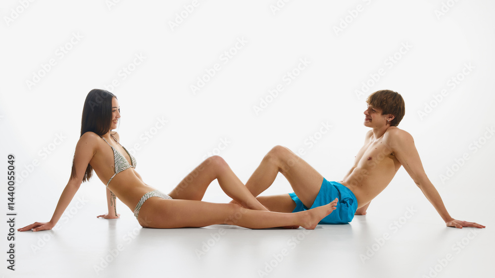 Obraz premium Happy, loving, smiling young man and woman, both in swimwear posing against white studio background. Concept of summer, fashion, youth culture, vacation. Banner. Copy space