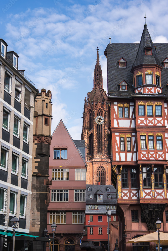 A street in Frankfurt, Germany, featuring the Gothic style Frankfurt Cathedral, a red and white half timbered building, and modern structures under a clear sky.