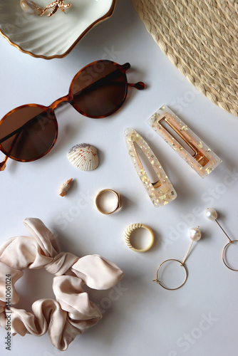 Sunglasses, straw hat, shells and jewelry in neutral colors. Seasonal summer accessories on white background. Flat lay.
