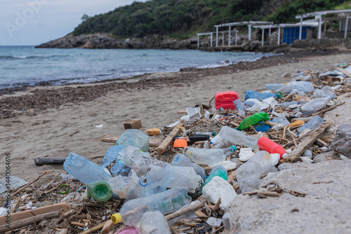 Large amount of plastic bottles, broken objects, and wooden debris covering sandy beach coastline. Ocean pollution and environmental degradation crisis.