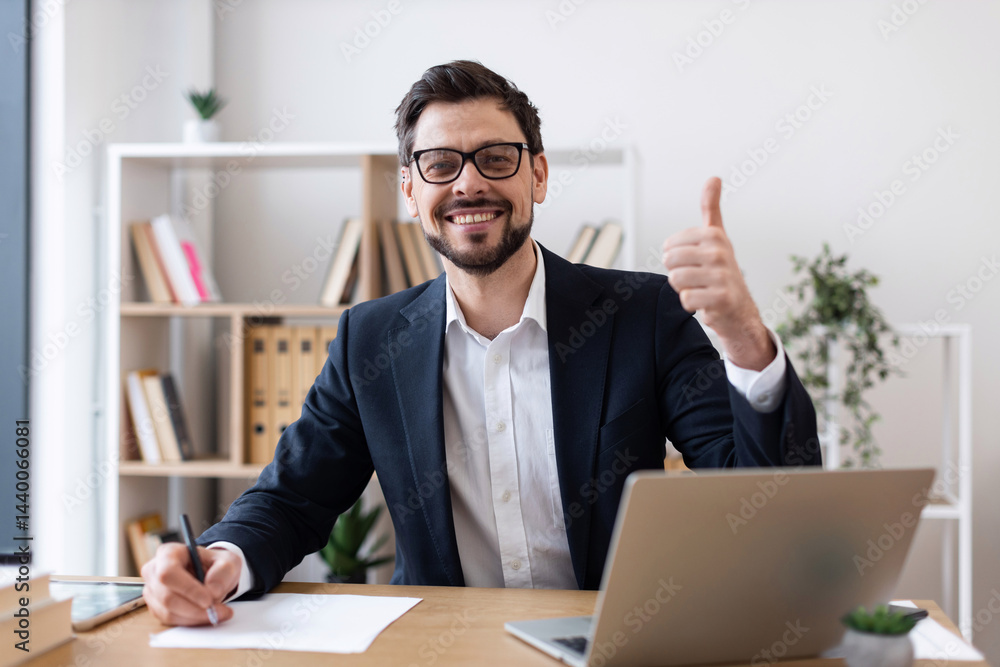 Professional adult male wearing suit working at desk smiling showing approval gesture thumbs up Professional adult male wearing suit working at desk smiling showing approval gesture thumbs up