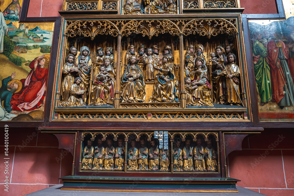 Intricately carved altarpiece in a Frankfurt church, featuring saints, angels, Gothic arches, and painted biblical panels against a red brick wall.