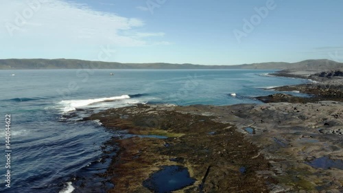Aerial view of rocky coast and fishing boat on northern sea under cloudy sky