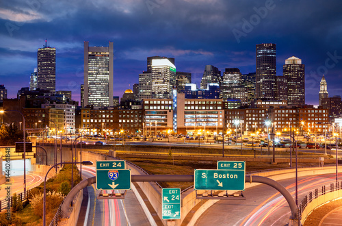 Obraz na płótnie A stunning nighttime view of Boston’s illuminated skyline with bright highway lights and dramatic clouds creating a vibrant urban atmosphere. w salonie