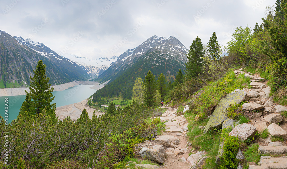 rocky alpine trail from Schlegeis dam lake upwards. green mountain pines and grey clouds