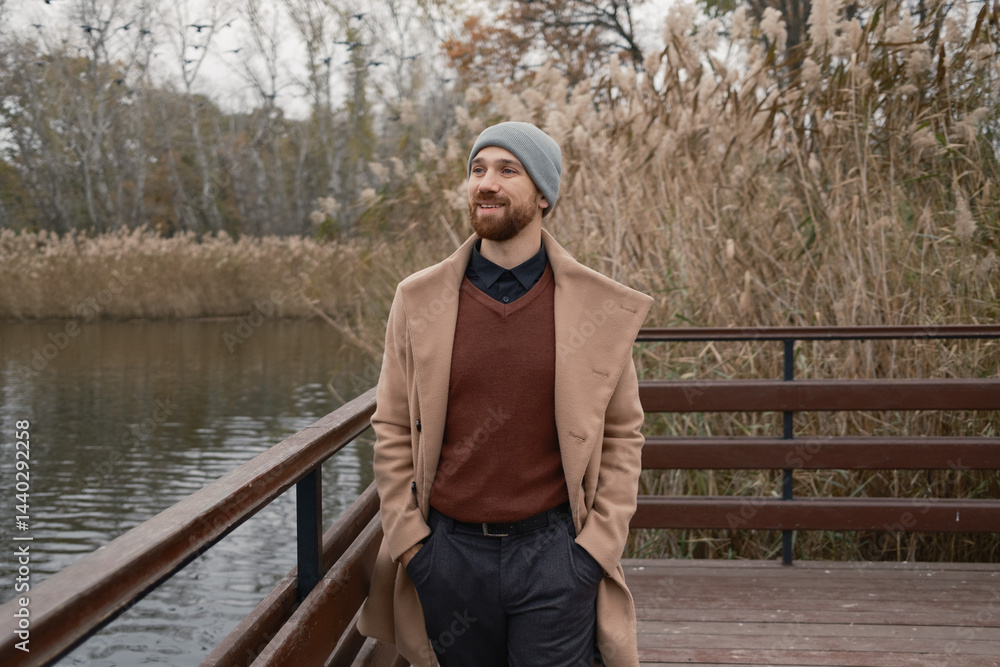 Bearded man in casual winter clothes outdoors near water surrounded by nature