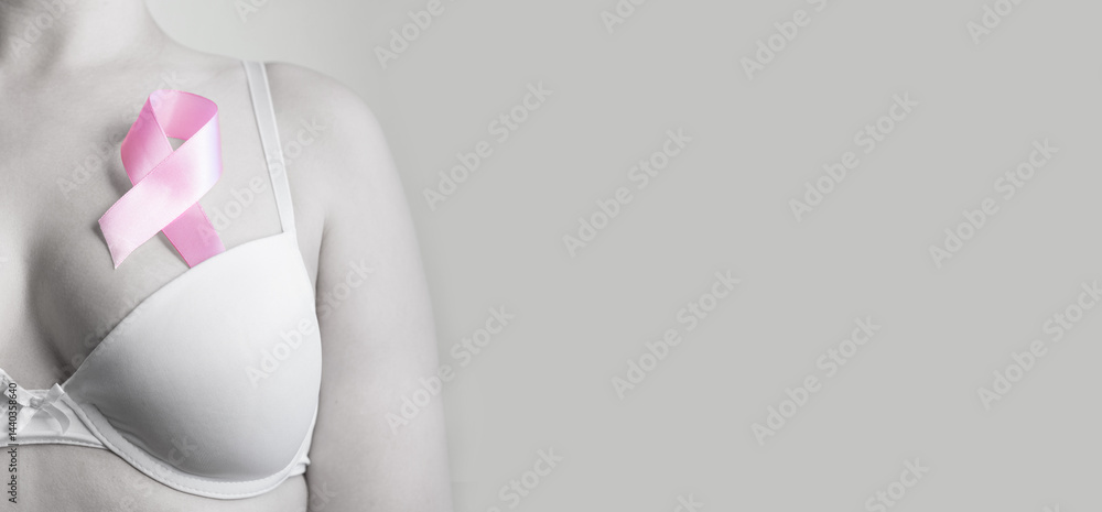 Woman in bra with pink ribbon on light background, closeup.