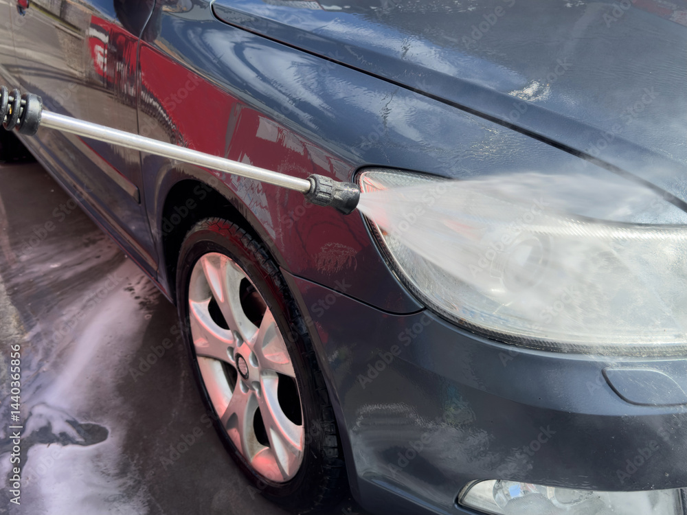 Close-up of car wash process. Man directing hose with water stream to his car, washing car at car wash.