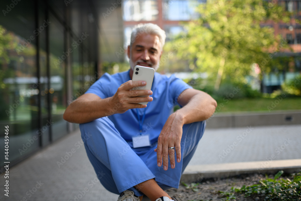 Healthcare worker outside hospital and checking phone during break. Healthcare worker outside hospital and checking phone during break.