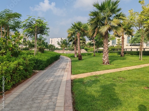 Small Interlock Path Between Landscaping Area. Green And Lush Landscaping Area With Carpet Grass And Trees Like Palm Or Washingtonia, Some Houses Or Villa's Also Beside Gardens Padestrian Pathway.
