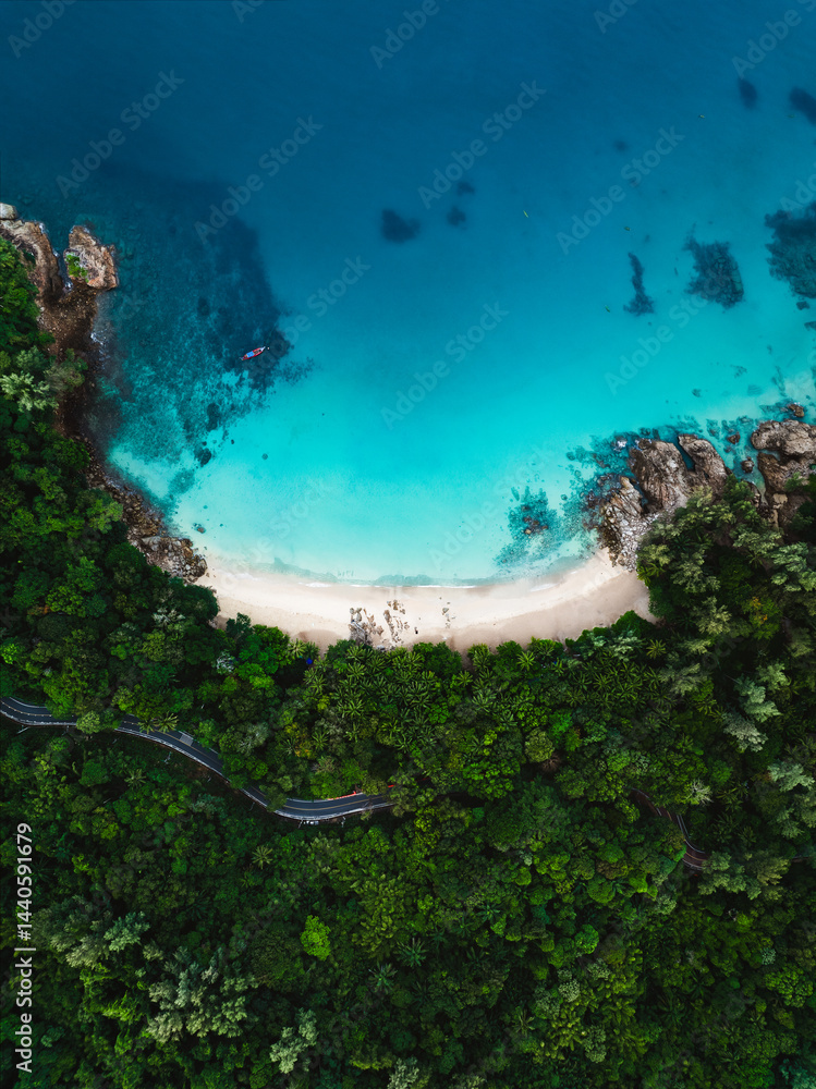 Vertical drone view of Banana Beach in Phuket, with lush tropical jungle, curvy road, and stunning turquoise waters.