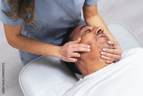 Female physiotherapist performing a relaxing facial massage on a male patient, providing personalized care and treatment