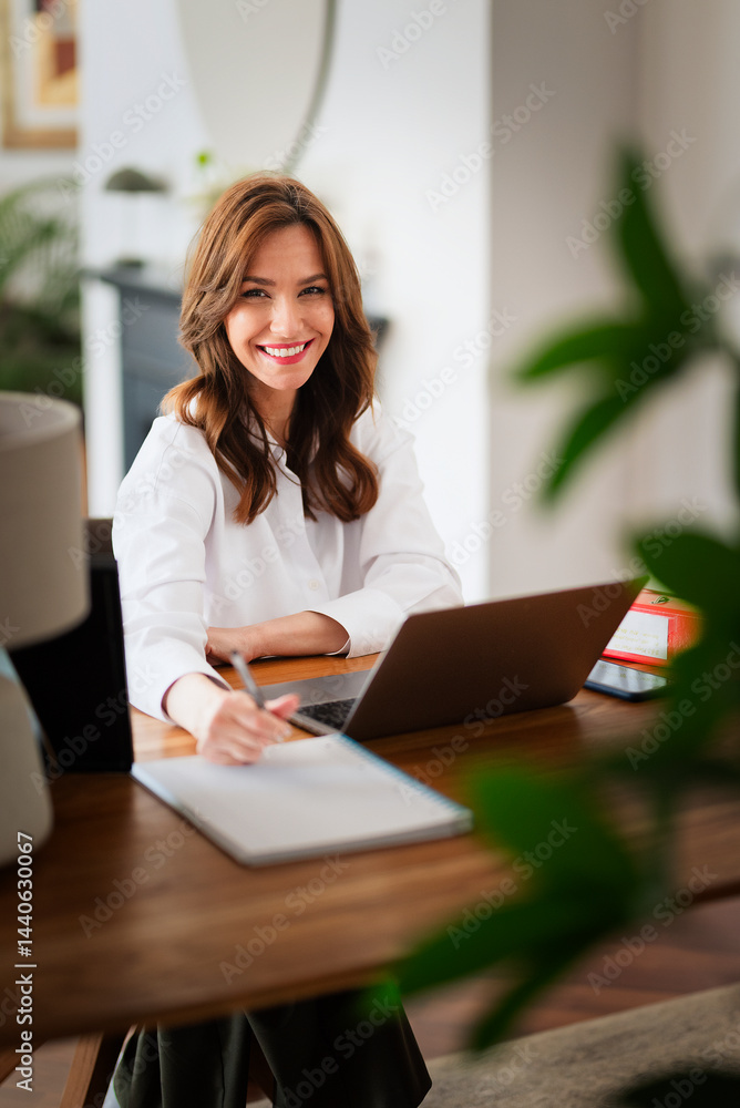 Confident woman sitting at desk and using her laptop while working from home Confident woman sitting at desk and using her laptop while working from home