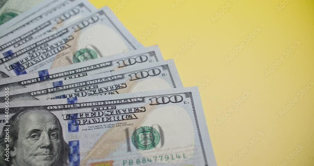 Close-up slide shot of neatly stacked $100 bills featuring Benjamin Franklin against vibrant yellow background. Crisp currency details with green seals and denomination clearly visible.
