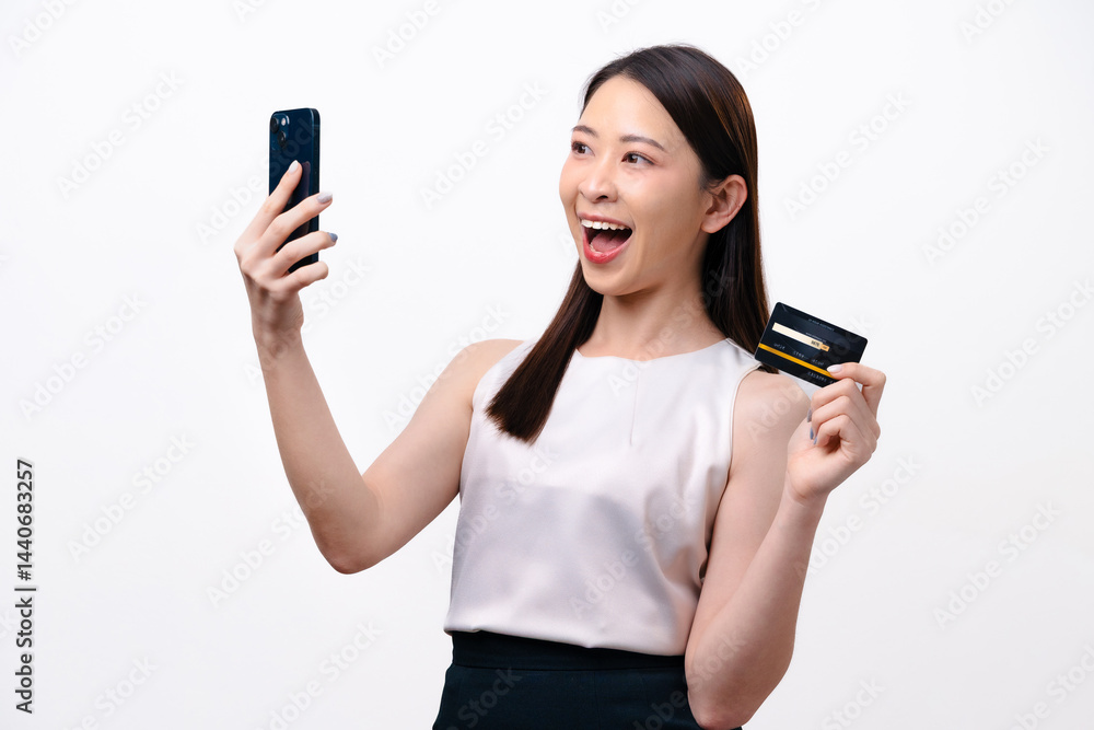 A beautiful young Asian businesswoman holds a credit card and a smartphone in her hand A beautiful young Asian businesswoman holds a credit card and a smartphone in her hand
