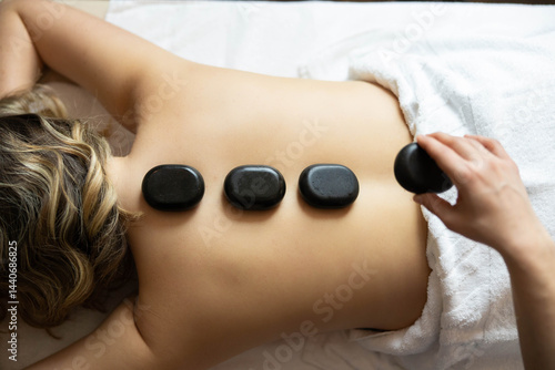 A close-up view of a hand placing a hot stone on a client's back, emphasizing the therapeutic experience of the massage.