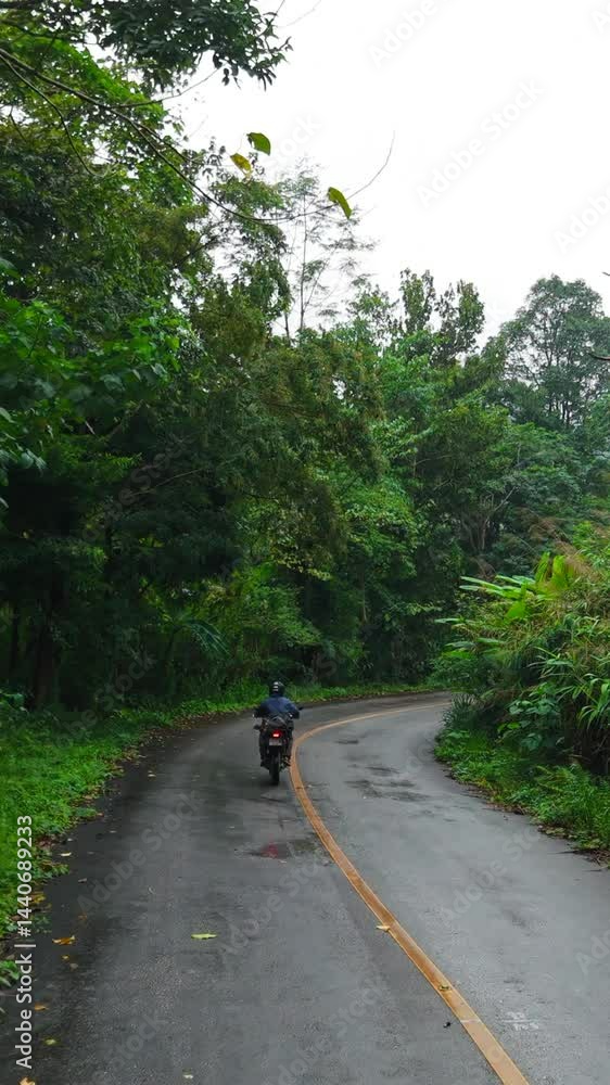 Motorcyclist riding a narrow winding road surrounded by vegetation in Mae Wong national park thailand Motorcyclist riding a narrow winding road surrounded by vegetation in Mae Wong national park thailand