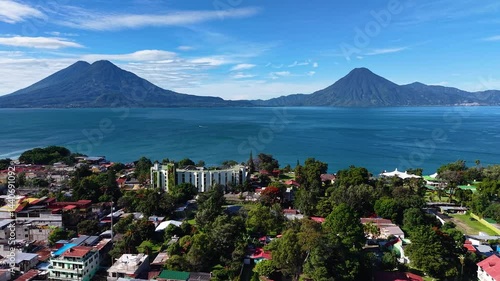Beautiful cinematic aerial view os the Panajachel town surrounded by Toliman and Atitlan volcanoes, next to the Atitlan lake its piers and traditional fisher and tourist boats - Guatemala