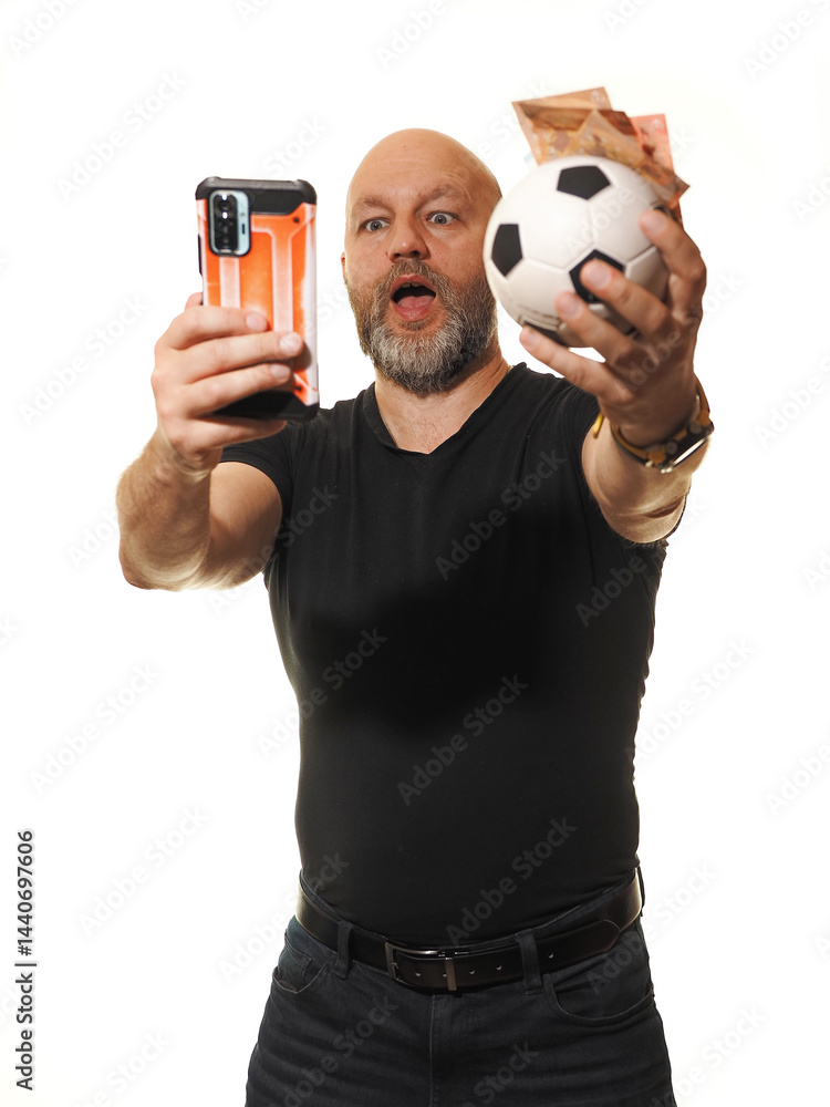 Betting on soccer or football concept. Adult male gambler in black shirt in his 50s holding ball and cash and phone, model with grey beard on white background. Making money on sport events concept.